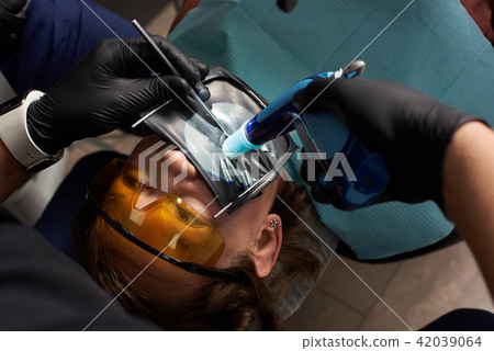 Dentist performs dental treatment to a patient in orange dental glasses with a rubberdam 42039064