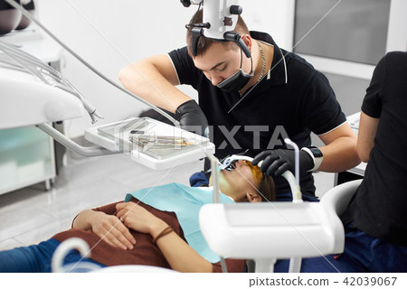 Male dentist in black uniform fixing young girl teeth with dental instruments Male dentist in black uniform fixing young girl teeth with dental instruments 42039067