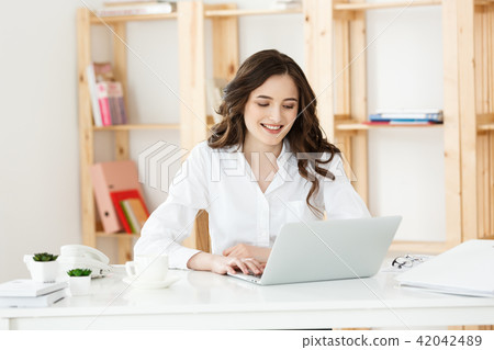 Smiling young woman sitting in front of notebook in the office. Smiling young woman sitting in front of notebook in the office. 42042489