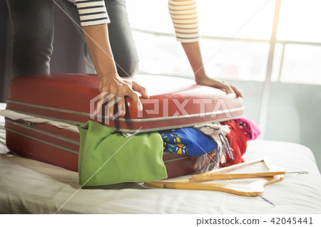 Woman trying to fit all clothing to packing her red suitcase be Woman trying to fit all clothing to packing her red suitcase be 42045441