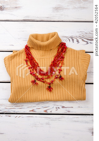 Folded yellow sweater with red necklace. Folded yellow sweater with red necklace. 42052564
