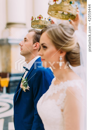 Newlyweds with the golden crowns under heads. The groom is in focus. 42059444