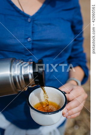 Woman pouring hot tea from a thermos on a sandy beach on a Sunny day. Close up. 42060561