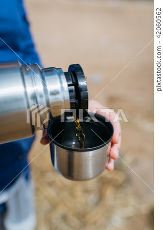 Woman pouring hot tea from a thermos on a sandy beach on a Sunny day. Close up. Woman pouring hot tea from a thermos on a sandy beach on a Sunny day. Close up. 42060562