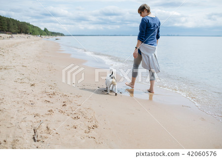 Woman walking with her dog on the sandy beach. Rear view. 42060576