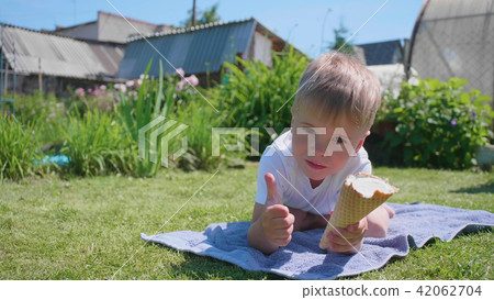 A little boy lying on the lawn and happy to eat ice cream. Hot summer day, cold sweet dessert A little boy lying on the lawn and happy to eat ice cream. Hot summer day, cold sweet dessert 42062704