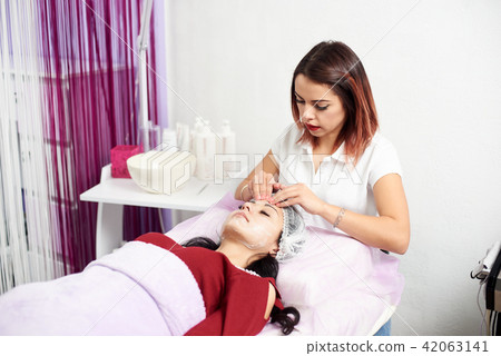 Cosmetologist applying cream to the face and massages woman Cosmetologist applying cream to the face and massages woman 42063141