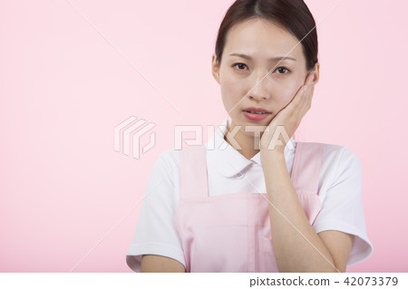 A woman wearing a white suit and a apron that puts her hand on her cheek and makes a troubled look A woman wearing a white suit and a apron that puts her hand on her cheek and makes a troubled look 42073379