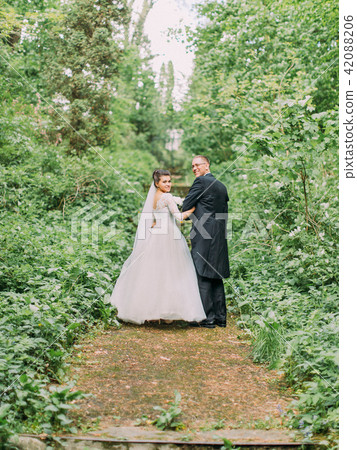 Walking newlywed couple along the road surrounded by green bushes. 42088206