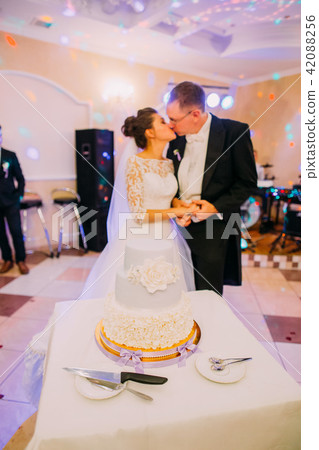 The white floral wedding cake at the background of the kissing newlywed couple. The white floral wedding cake at the background of the kissing newlywed couple. 42088256