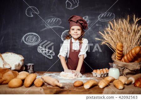 Little girl kneading dough at table 42092563
