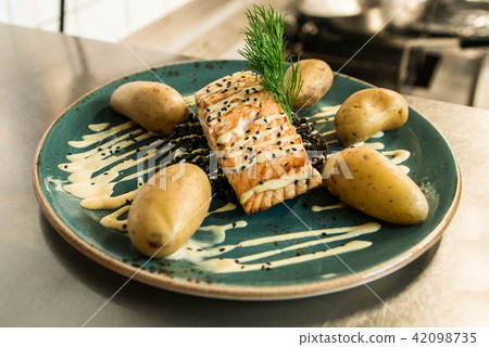 grilled salmon placed on a plate with black bulgur and with cooked potatoes arranged for dinner grilled salmon placed on a plate with black bulgur and with cooked potatoes arranged for dinner 42098735