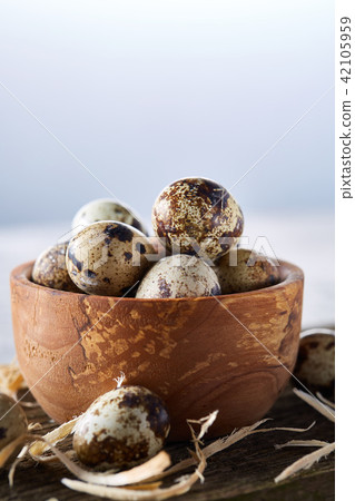 Wooden bowl filled with quail eggs on wooden board over white background, close-up, selective focus. Wooden bowl filled with quail eggs on wooden board over white background, close-up, selective focus. 42105959