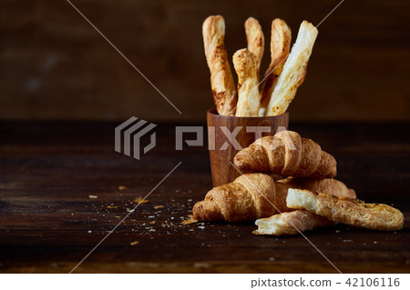 Puff pastries on piece of board over dark wooden table, close-up, selective focus, backlight. Puff pastries on piece of board over dark wooden table, close-up, selective focus, backlight. 42106116