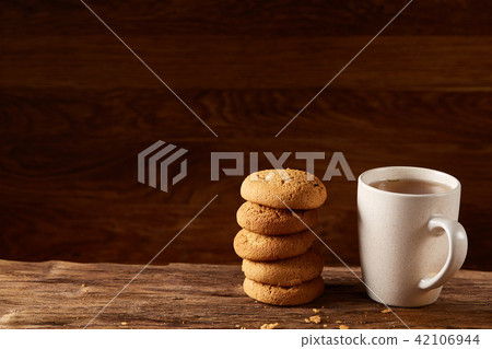 White porcelain mug of tea and sweet cookies on piece of wood over wooden background, top view 42106944