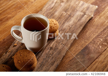 White porcelain mug of tea and sweet cookies on piece of wood over wooden background, top view White porcelain mug of tea and sweet cookies on piece of wood over wooden background, top view 42106948