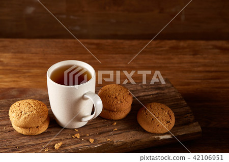 White porcelain mug of tea and sweet cookies on piece of wood over wooden background, top view 42106951