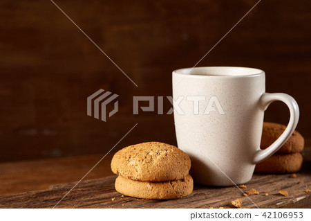 White porcelain mug of tea and sweet cookies on piece of wood over wooden background, top view White porcelain mug of tea and sweet cookies on piece of wood over wooden background, top view 42106953
