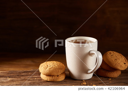 White porcelain mug of tea and sweet cookies on piece of wood over wooden background, top view White porcelain mug of tea and sweet cookies on piece of wood over wooden background, top view 42106964
