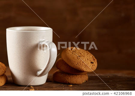 White porcelain mug of tea and sweet cookies on piece of wood over wooden background, top view White porcelain mug of tea and sweet cookies on piece of wood over wooden background, top view 42106968