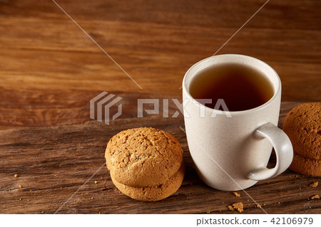 White porcelain mug of tea and sweet cookies on piece of wood over wooden background, top view 42106979