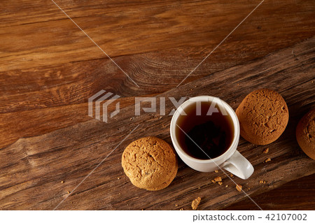 White porcelain mug of tea and sweet cookies on piece of wood over wooden background, top view White porcelain mug of tea and sweet cookies on piece of wood over wooden background, top view 42107002