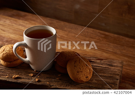 White porcelain mug of tea and sweet cookies on piece of wood over wooden background, top view 42107004