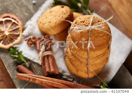 Christmas composition with pile of cookies, cinnamon and dried oranges on light wooden background Christmas composition with pile of cookies, cinnamon and dried oranges on light wooden background 42107049