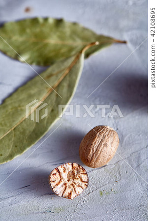 Bay leaf and nutmeg on white textured background, top view, close-up, selective focus, vertical. 42108695