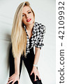 beautiful young blond woman posing while leaning on interior studio wall. 42109932
