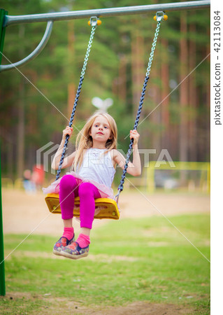 Little blonde girl swinging outdoors on playground Little blonde girl swinging outdoors on playground 42113084