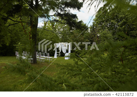 Wedding ceremony in the open air.Transparent chairs with fluttering ribbons in the Park or forest 42113872