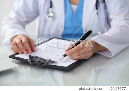 Doctor woman filling up medical form while sitting at the table, close-up of hands 42117677