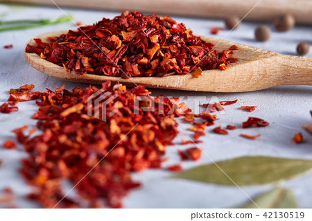 Red hot chillies pepper flakes in wooden spoon on white textured background, top view, close-up Red hot chillies pepper flakes in wooden spoon on white textured background, top view, close-up 42130519