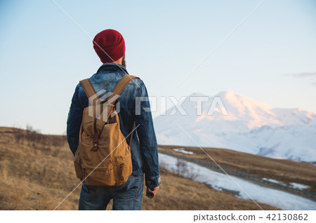 Bearded tourist hipster man in a hat with a backpack stand back on a roadside bump and watching the 42130862