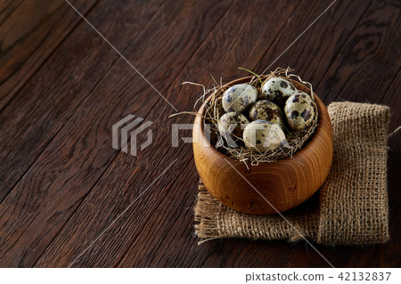 Fresh quail eggs in a wooden bowl on a dark wooden background, top view, close-up Fresh quail eggs in a wooden bowl on a dark wooden background, top view, close-up 42132837