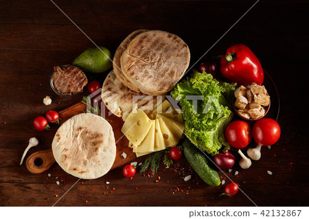 Plain pita on a cutting board with fresh vegetables and cheese on a wooden background, flat lay Plain pita on a cutting board with fresh vegetables and cheese on a wooden background, flat lay 42132867