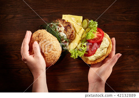 Woman's hands holding traditional american burger on wooden background, top view, close-up. Woman's hands holding traditional american burger on wooden background, top view, close-up. 42132889