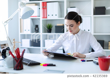 A young girl sits in the office, holds a pen in her hand and looks through documents. 42135369