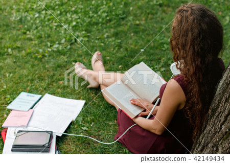 girl student holding book and sitting under tree girl student holding book and sitting under tree 42149434