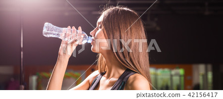 Fitness young woman drinking water in the gym. Muscular woman taking break after exercise 42156417