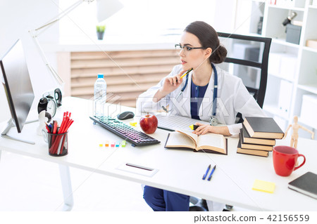 A beautiful young girl in a white robe sits at a table, holds a marker and a pen in her hand and 42156559