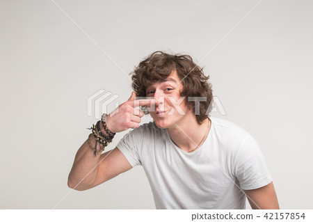 Studio portrait of funny young man pointing on his nose in white t-shirt Studio portrait of funny young man pointing on his nose in white t-shirt 42157854