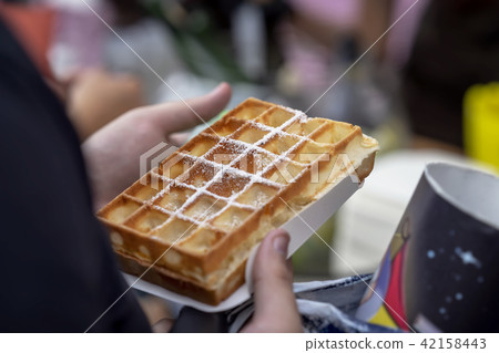 Belgian fresh warm waffle with powdered sugar in hands of buyer. Gastronomic dainty products on 42158443