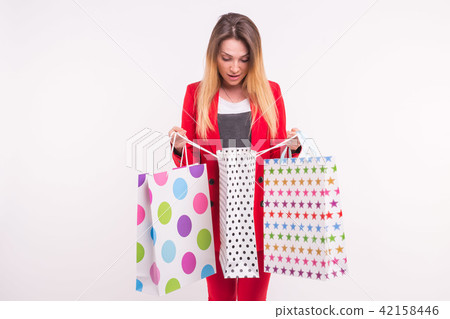 Tender young woman with shopping bags in red suit is posing on white background with copy space. Tender young woman with shopping bags in red suit is posing on white background with copy space. 42158446