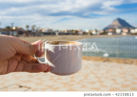 Cup of coffee in hand on the background of a beautiful beach. Cup of coffee in hand on the background of a beautiful beach. 42158613
