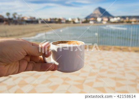 Cup of coffee in hand on the background of a beautiful beach. Cup of coffee in hand on the background of a beautiful beach. 42158614