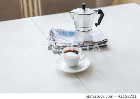 Vintage coffee pot, a cup of coffee is on a white table Vintage coffee pot, a cup of coffee is on a white table 42158721