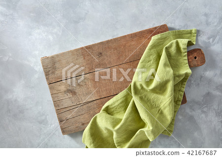 A wooden board with a green kitchen napkin on a gray concrete background with a copy space. Top view 42167687