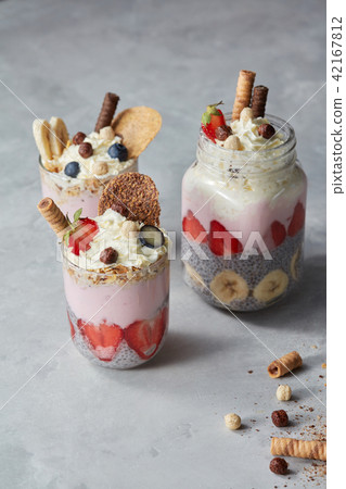 Colorful layered smoothie with berries, biscuits and whipped cream in jar on a stone background Colorful layered smoothie with berries, biscuits and whipped cream in jar on a stone background 42167812